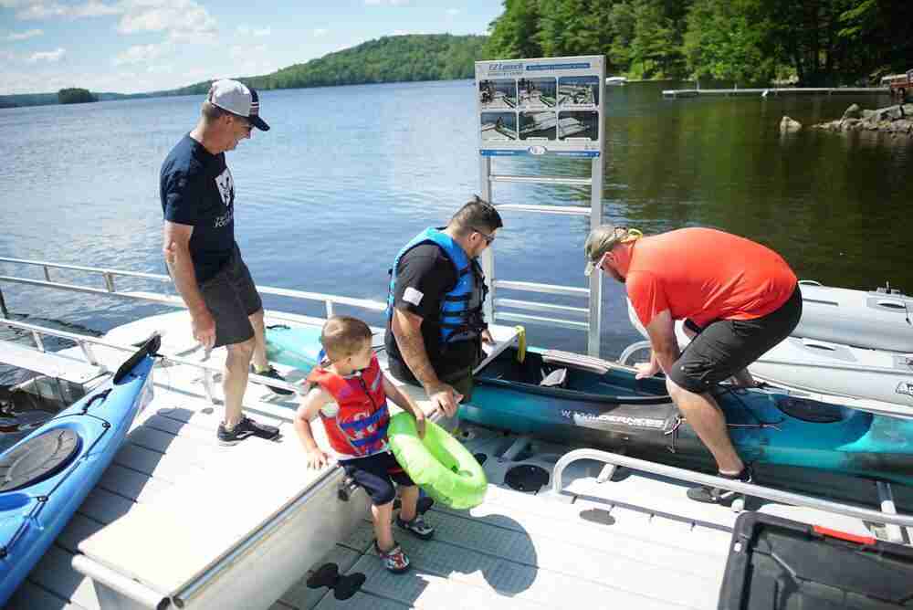 two men helping a disabled veteran getting into a kayak while his child waits nearby