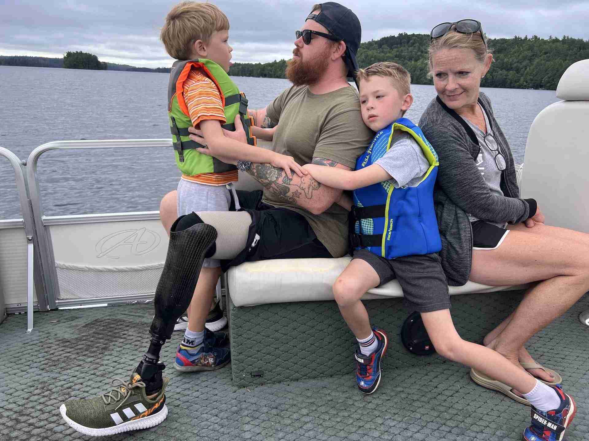 two young boys sitting on their dads lap while their mom looks at them, all sitting on a boat on a lake